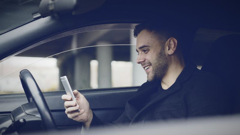 Man in a car smiling at his smartphone
